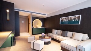 Een moderne woonkamer met een bank, een poef en een ronde salontafel. Er hangt een kunstwerk aan de muur en boven de bank een ronde lamp.