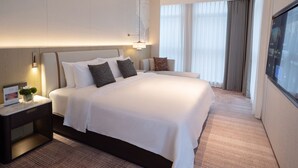 Een hotelkamer met een groot bed, een nachtkastje met een lamp en uitzicht op de stad door het raam.