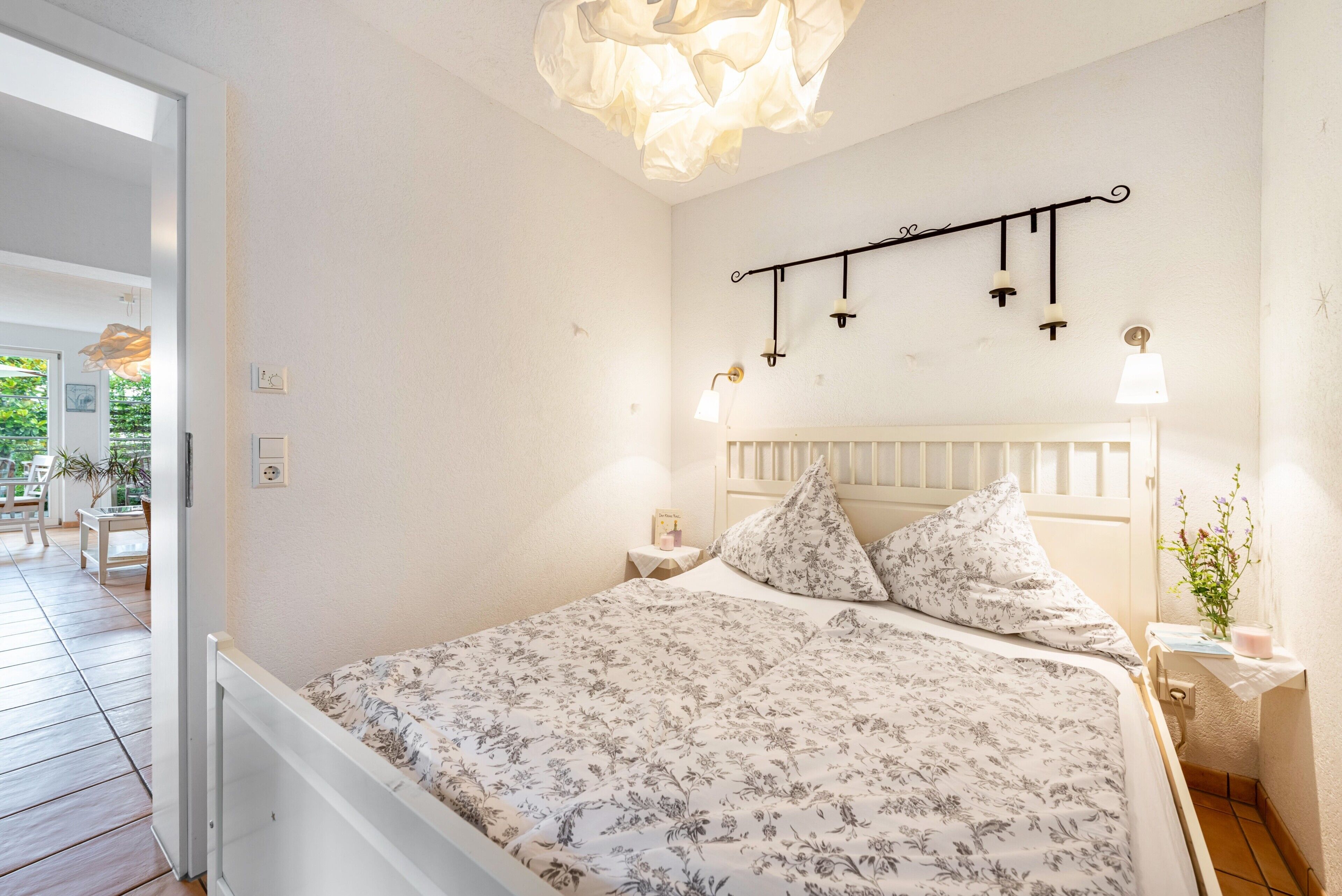 Un dormitorio con cama, mesita de noche, lámpara de pared y ventana.