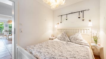 Un dormitorio con cama, mesita de noche, lámpara de pared y ventana.
