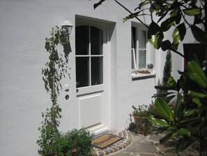 A white house with a white door, a window, and a small shelf with a plant.