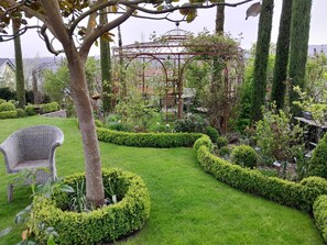 En trädgård med en pergola, välklippta häckar och en flätad stol.