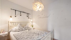 A bedroom with a white bed, floral bedding, a bedside table with a lamp, and a wall-mounted light fixture. - Apartment 'Romantica' with Lake View, Private Terrace and Wi-Fi (Sipplingen)
