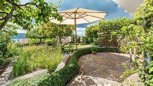 A patio area with a stone pathway, a large umbrella, and lush greenery. - Apartment 'Romantica' with Lake View, Private Terrace and Wi-Fi (Sipplingen)