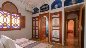 A bedroom with a bed, a window with stained glass, and a hallway with wooden doors. - Riad Safran – Private Chef, Indoor Pool Gem (Marrakesh)