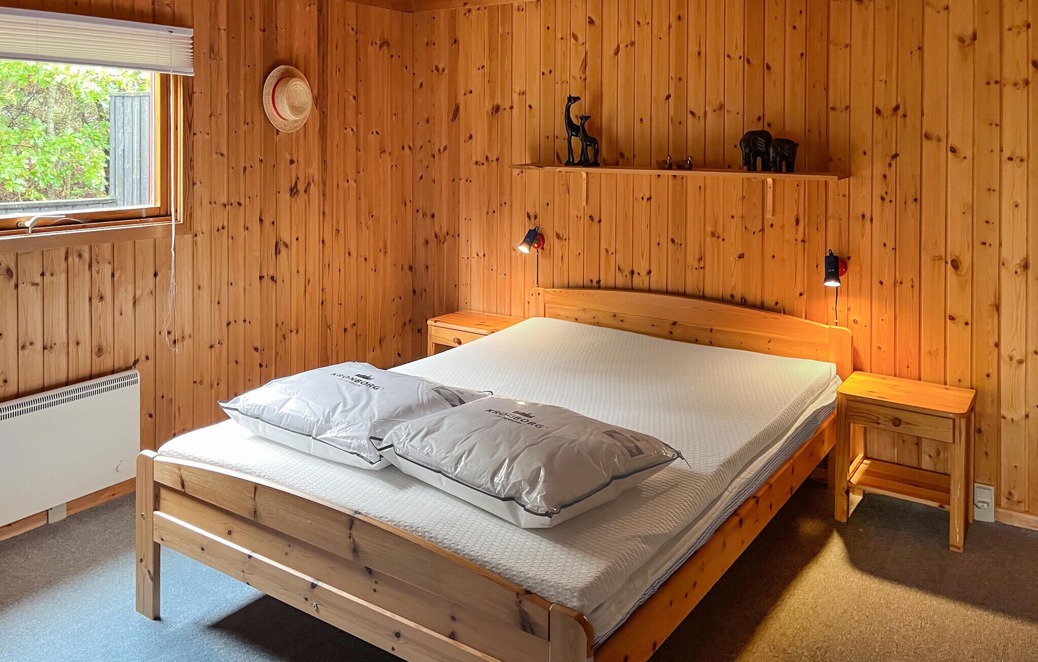 Ein Schlafzimmer mit Holzvertäfelung, einem Bett, zwei Nachttischen, einem Fenster und einem Regal mit Dekorationen.