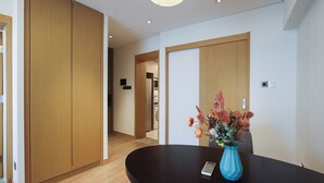 Zona de recepción de hotel con un mostrador oscuro, un jarrón azul con flores, puertas de madera y un pasillo que da a otras habitaciones.
