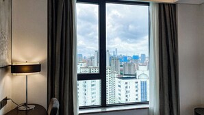 Una habitación de hotel con un ventanal grande, un escritorio con lámpara y una cama.