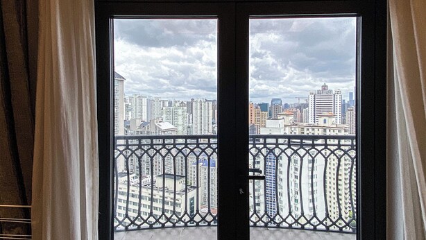 Un balcón con vista a un paisaje urbano a través de una puerta de vidrio con marco negro.