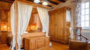 A wooden cabin interior with a bed, a wooden dresser, a chair, and a large mirror.