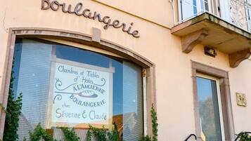 Un bâtiment avec une enseigne indiquant « Boulangerie » et une vitrine où est affiché un panneau publicitaire pour « Chambres et Tables d’hôtes à l’ancienne chez Boulangerie Séverine et Claude ».