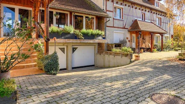 A residential street with houses, a garage, and a cobblestone driveway.