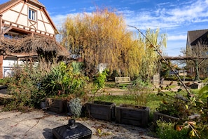 A garden with a bench, wooden planters, and a house with a sloped roof. - Guest Room & Table d'Hôtes 'À L'ancienne Boulangerie - Épeautre' (Elsenheim)