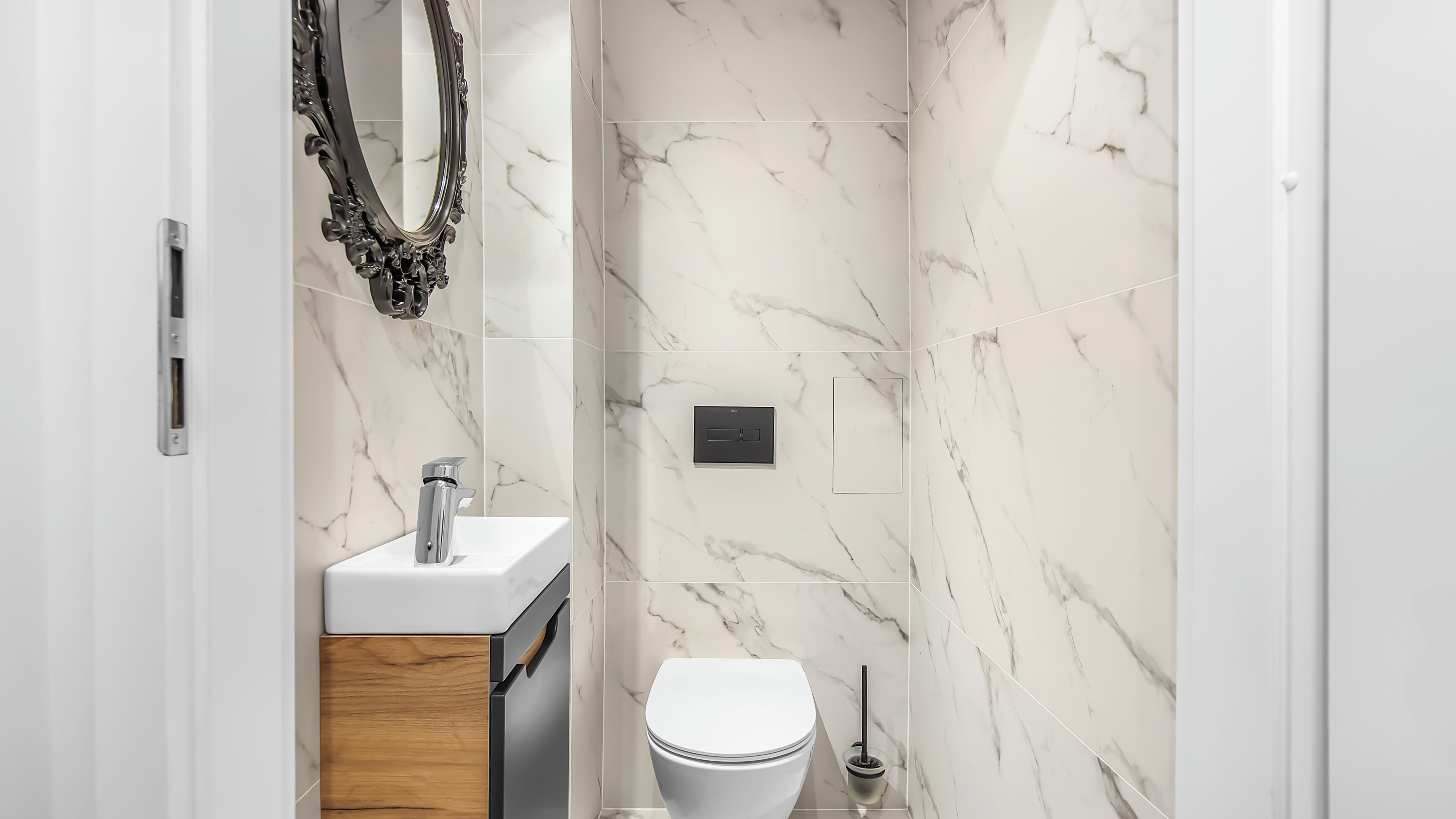 A modern bathroom with a marble backsplash, a white sink, a toilet, and a shower area.