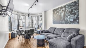 A modern living room with a gray sofa, a round glass coffee table, and a dining area with a round table and chairs. - Apartamenty Sun & Snow Rozbrat Ołbin (Wrocław)