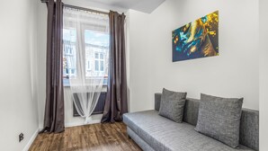 A room with a grey sofa, a painting, and a window with curtains. - Apartamenty Sun & Snow Rozbrat Ołbin (Wrocław)