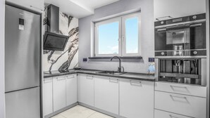 A modern kitchen with a built-in oven, a stainless steel refrigerator, a marble backsplash, and a window above the sink. - Apartamenty Sun & Snow Rozbrat Ołbin (Wrocław)