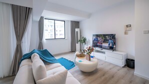 A modern living room with a sofa, a coffee table, a flat-screen TV, and a large window with curtains.