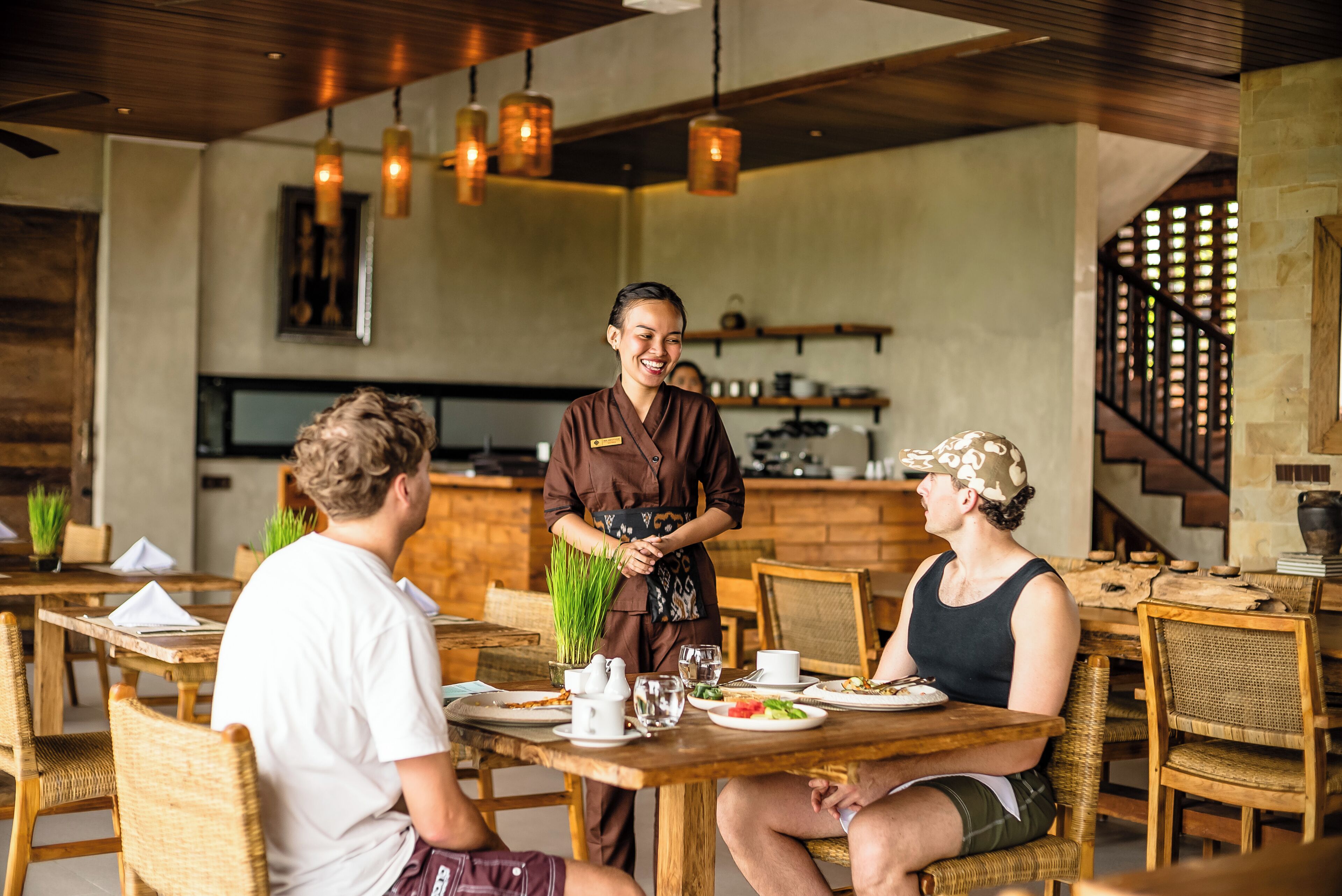 A restaurant with wooden tables and chairs, a bar area, and hanging pendant lights.