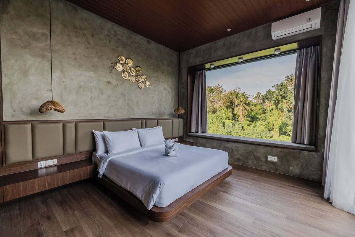 A modern bedroom with a large bed, a view of greenery, and a unique wall decoration.