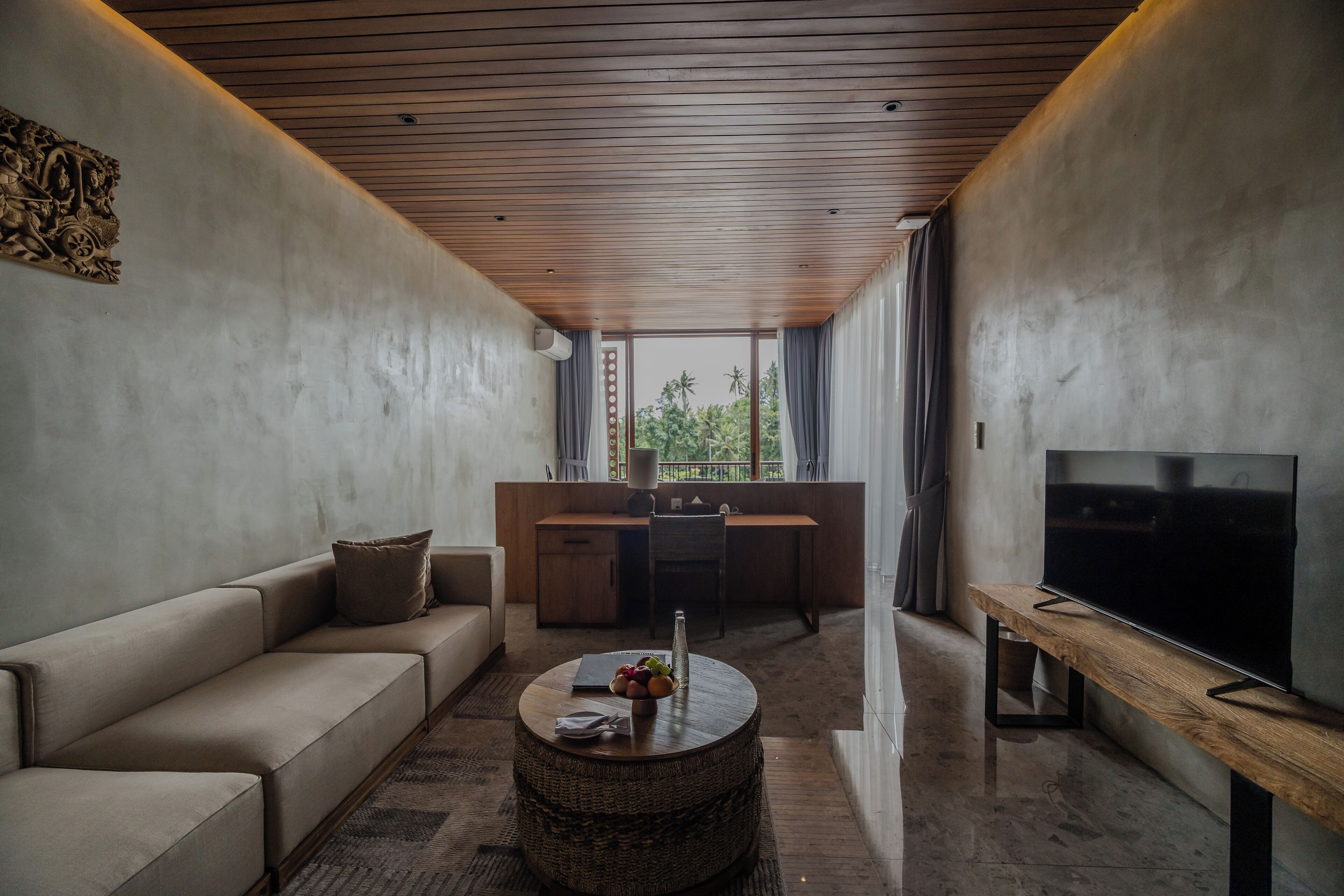 Una sala de estar moderna con sofá, una mesa de centro redonda, televisor y una zona de cocina al fondo.