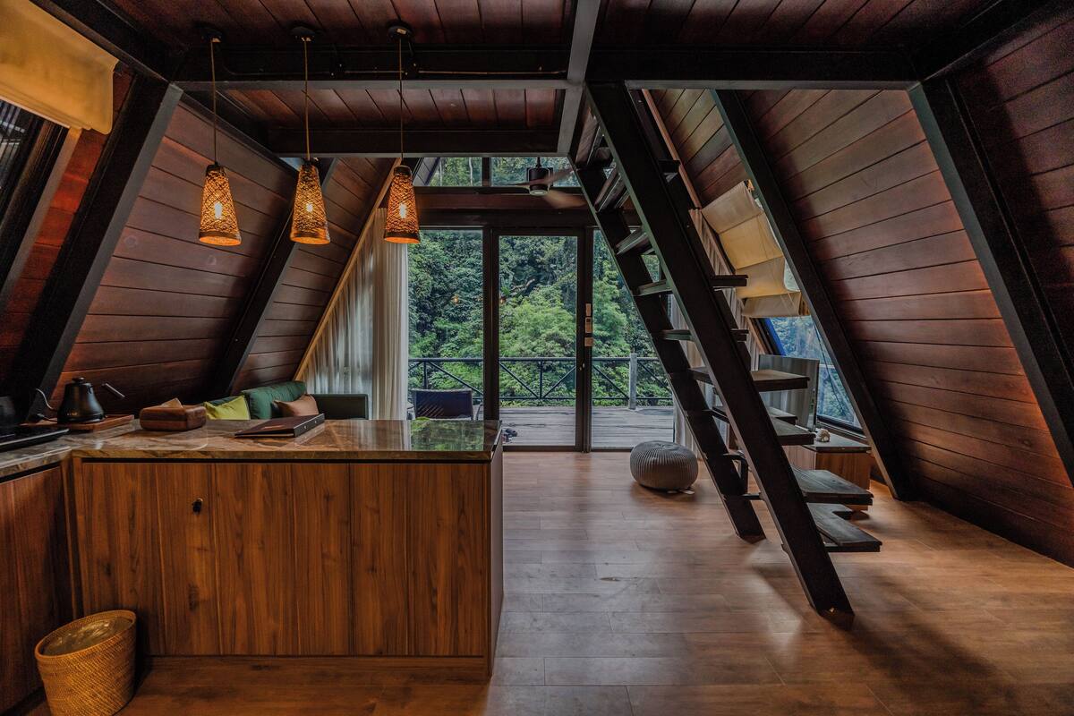 A modern kitchen with wooden cabinetry, a central island, pendant lighting, and a view of the outdoors through large windows.