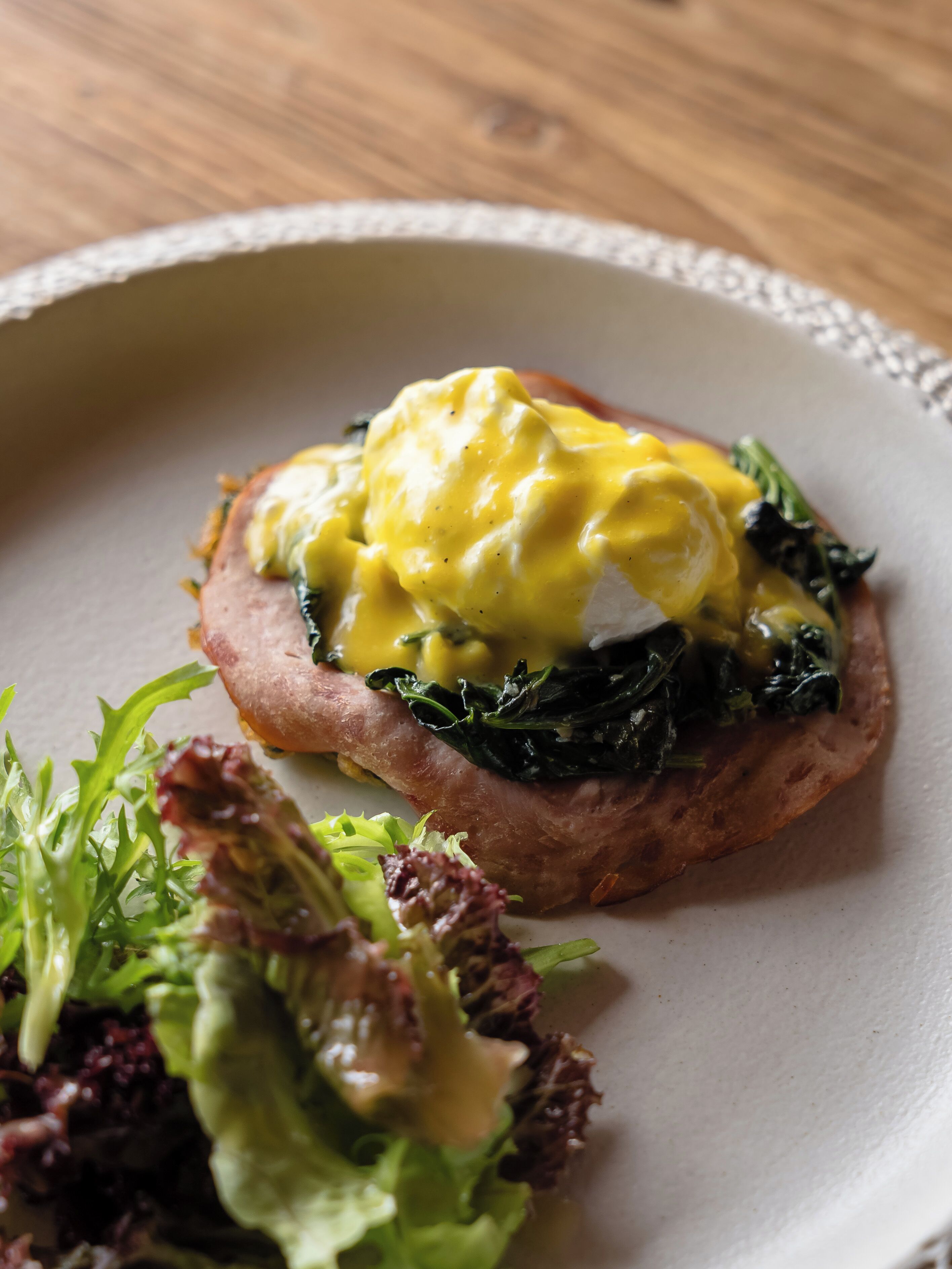 A plate with a sandwich topped with egg and spinach, accompanied by a side salad.