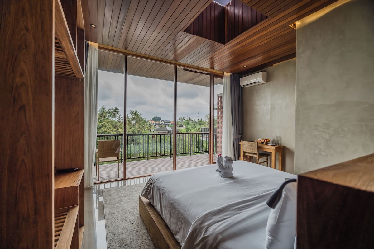A modern hotel room with a large bed, wooden ceiling, and a balcony with a view of greenery.