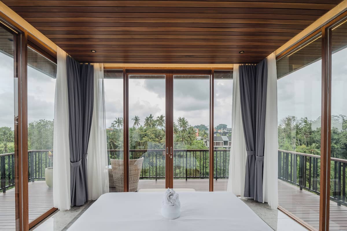 A spacious balcony with a wooden ceiling and large glass doors, offering a view of lush greenery and distant buildings.