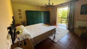 A bedroom with a bed, a dresser, a chandelier, a window with curtains, and a view of greenery outside. - House with private garden and mountain views (Cutigliano)