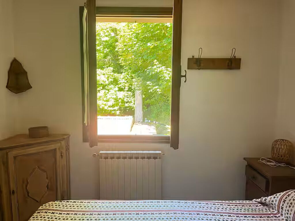 A bedroom with a bed, a radiator, a wooden cabinet, and a window with a view of trees.
