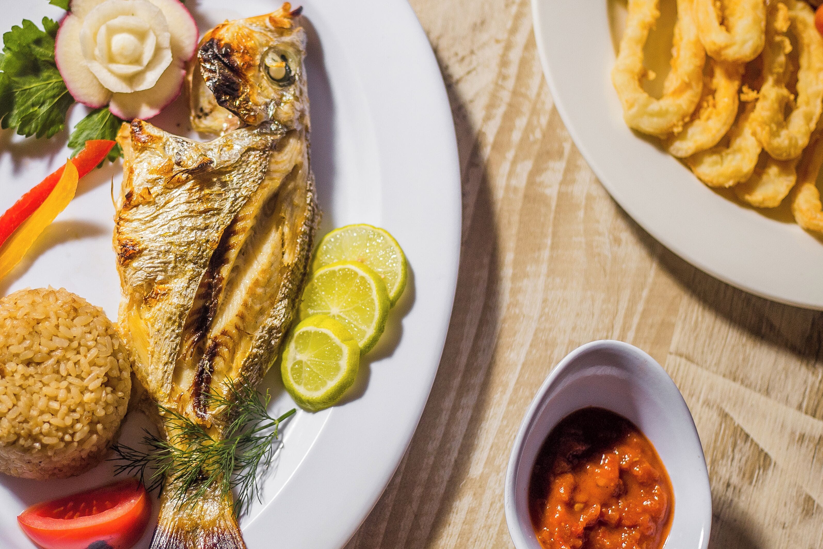 A plate with grilled fish, lime slices, and a side of rice.