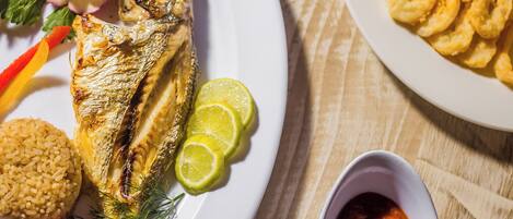 A plate with grilled fish, lime slices, and a side of rice.