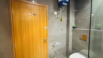 A bathroom with a wooden door, a shower with a glass enclosure, a toilet, and a water heater mounted on the wall.