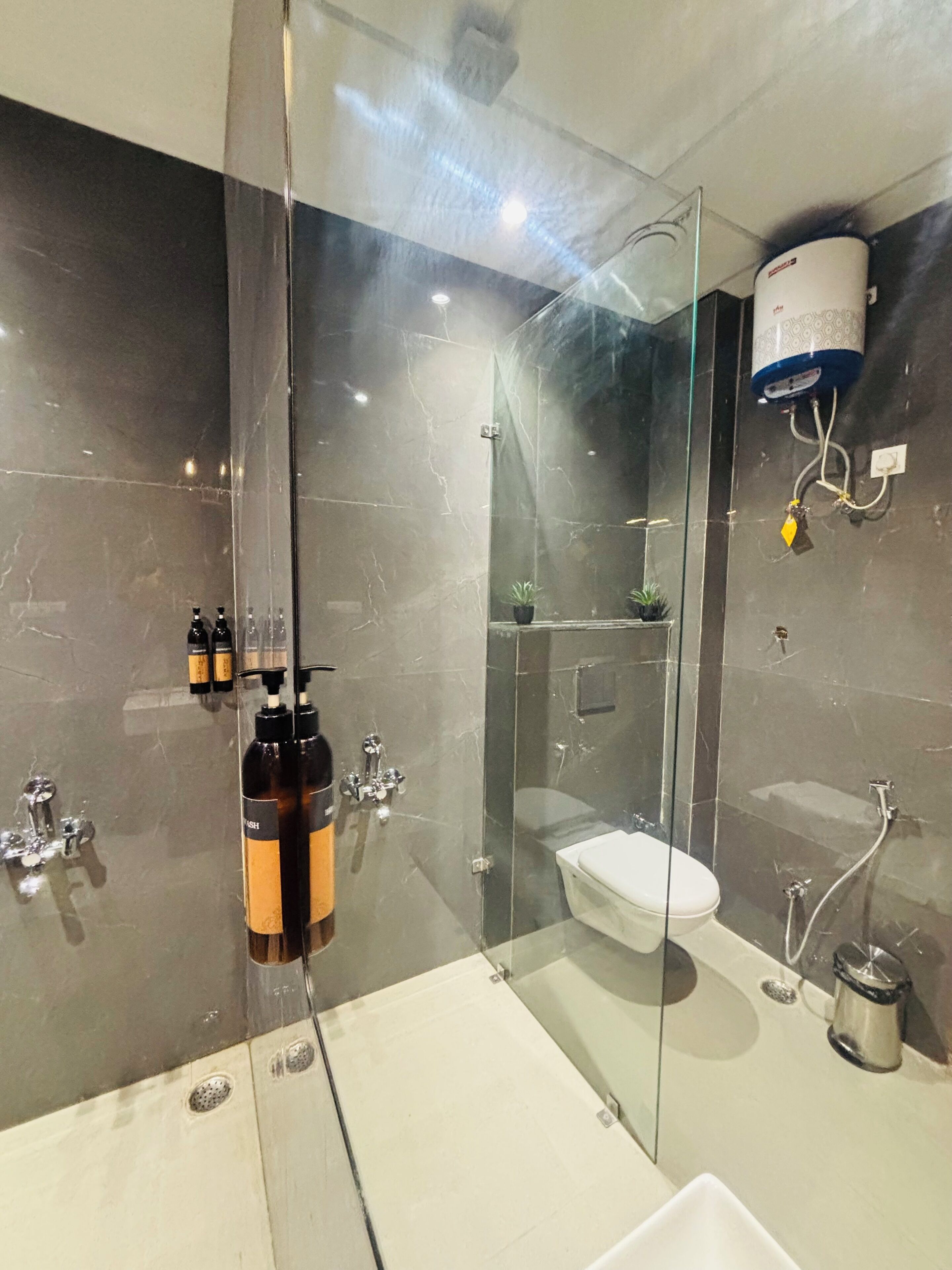 Un baño moderno con ducha de vidrio, un lavabo blanco y un inodoro. Hay dos botellas de champú y acondicionador sobre el lavabo.