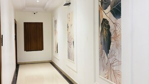 A hallway with a wooden door, white walls, and artwork. - Arth Suites Lucknow Gomti Nagar (Lucknow)