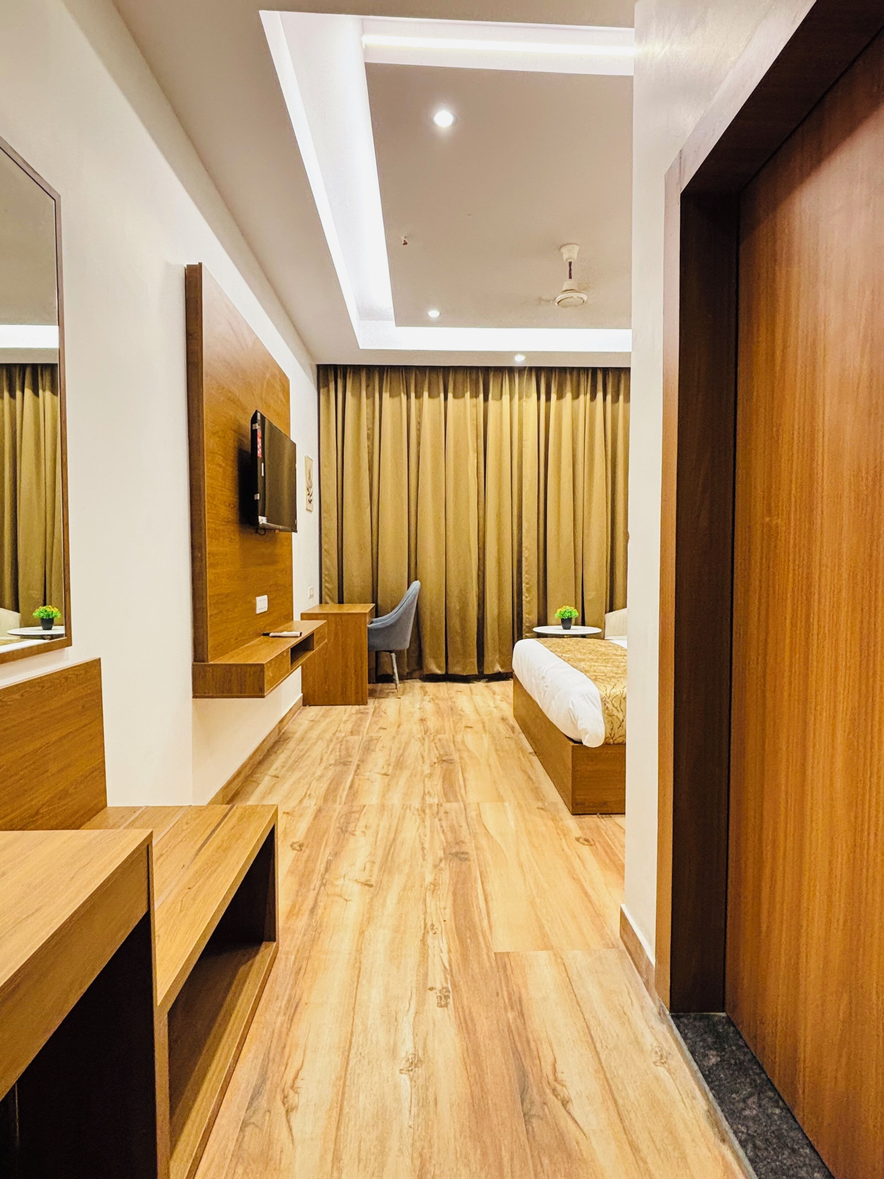 Una habitación de hotel moderna con piso de madera, una cama, un escritorio, una silla, un televisor y un ventilador de techo.