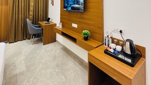 A modern hotel room with a wooden desk, a TV mounted on a wooden panel, a seating area with a chair, and a coffee maker on a side table. - Arth Suites Lucknow Gomti Nagar (Lucknow)
