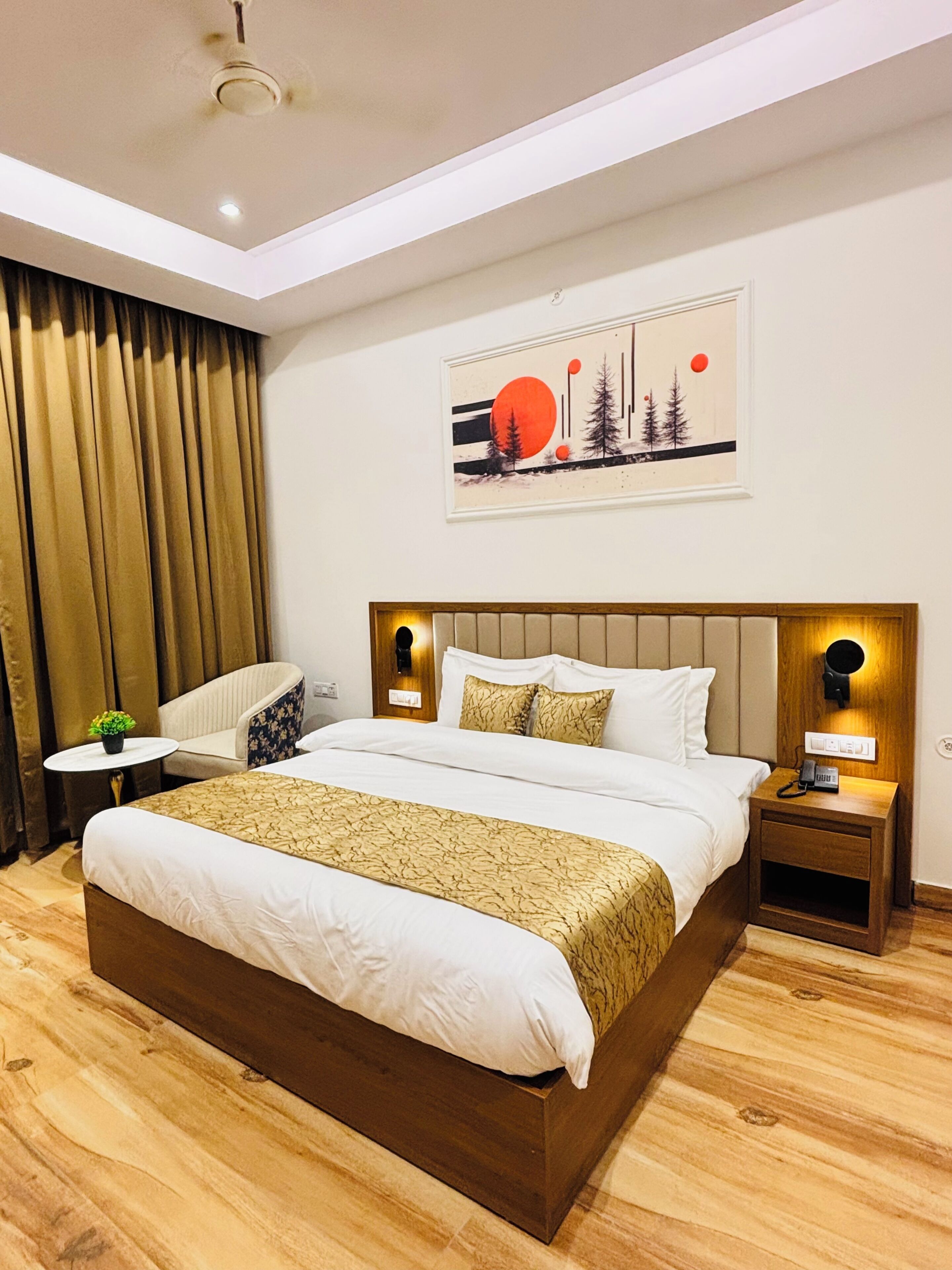 A hotel room with a large bed, a chair, a small table, and a painting on the wall.