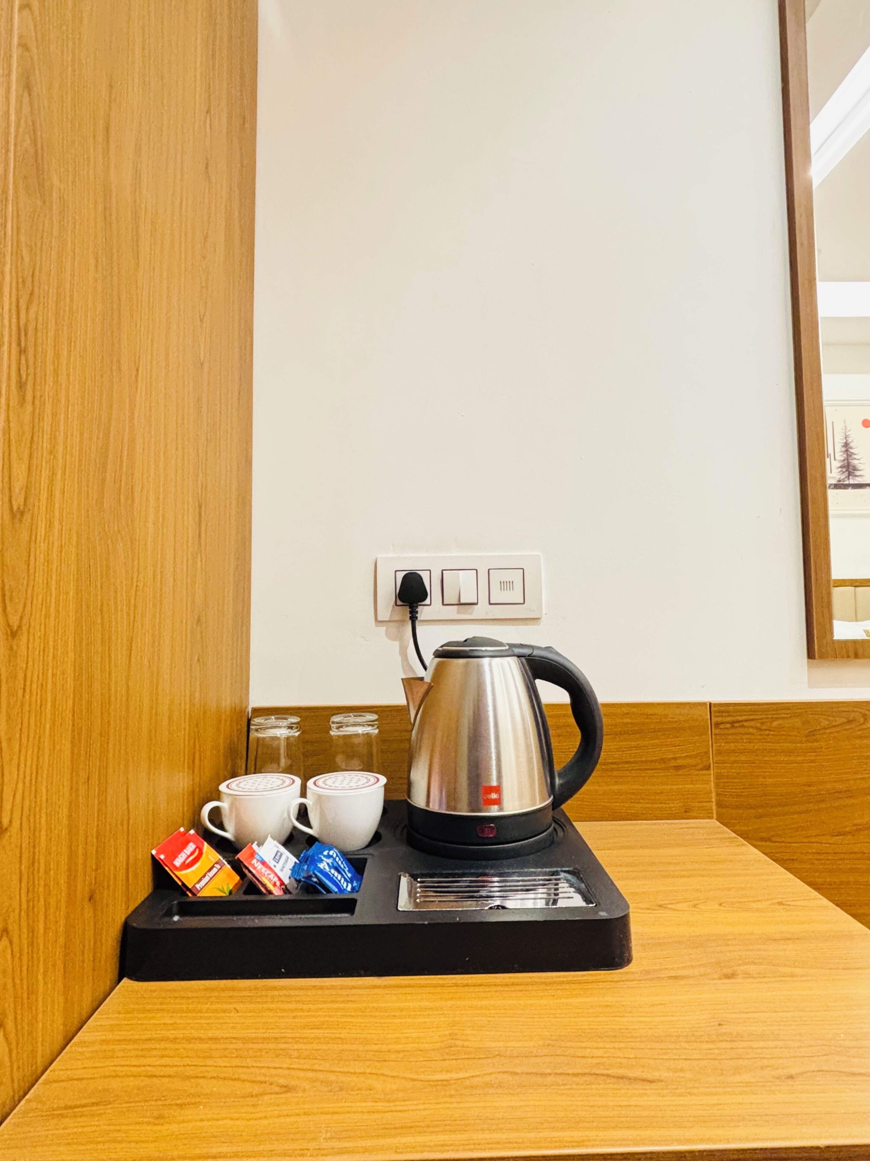 A coffee station with a kettle, cups, and sugar packets on a tray.