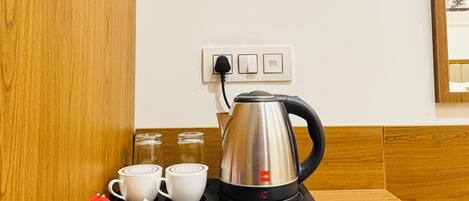 A coffee station with a kettle, cups, and sugar packets on a tray.