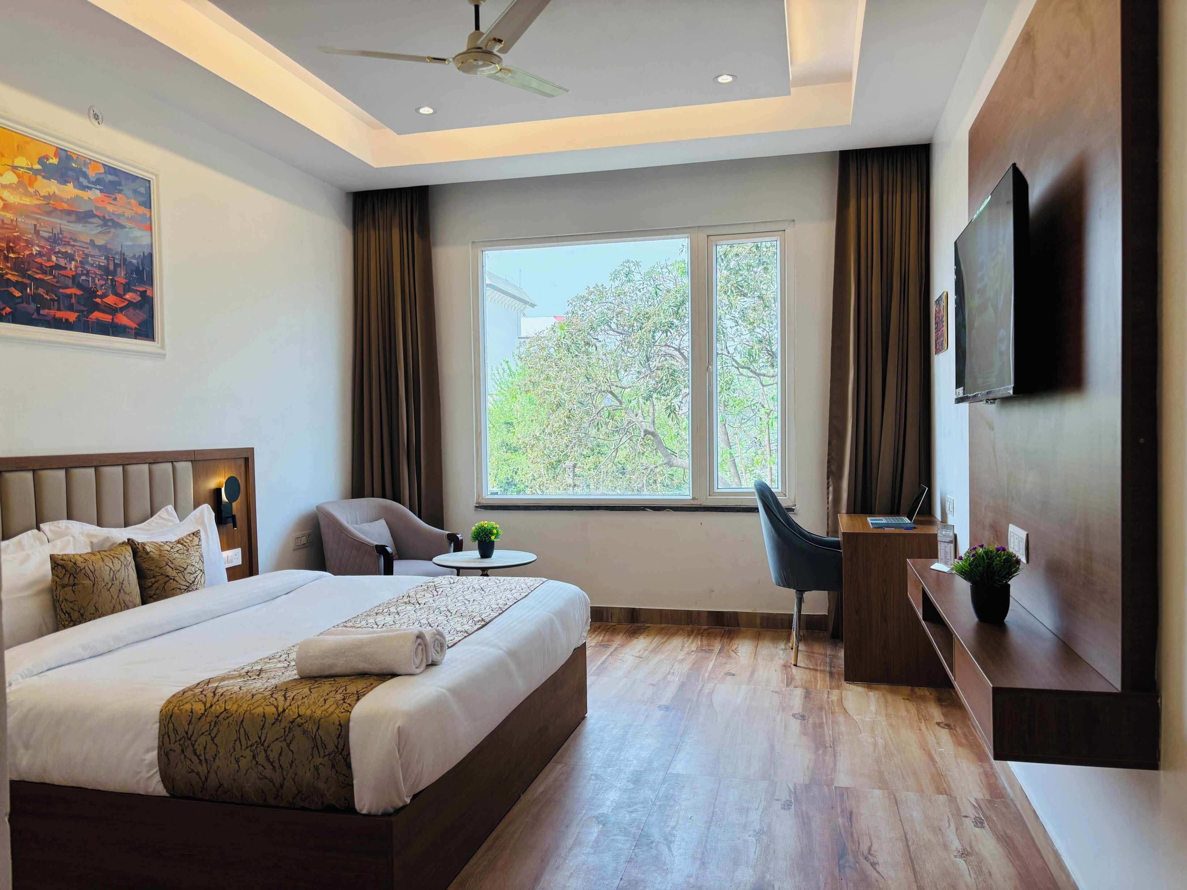 Habitación de hotel con una cama grande, un escritorio, una silla, un televisor y una ventana con vista a árboles.