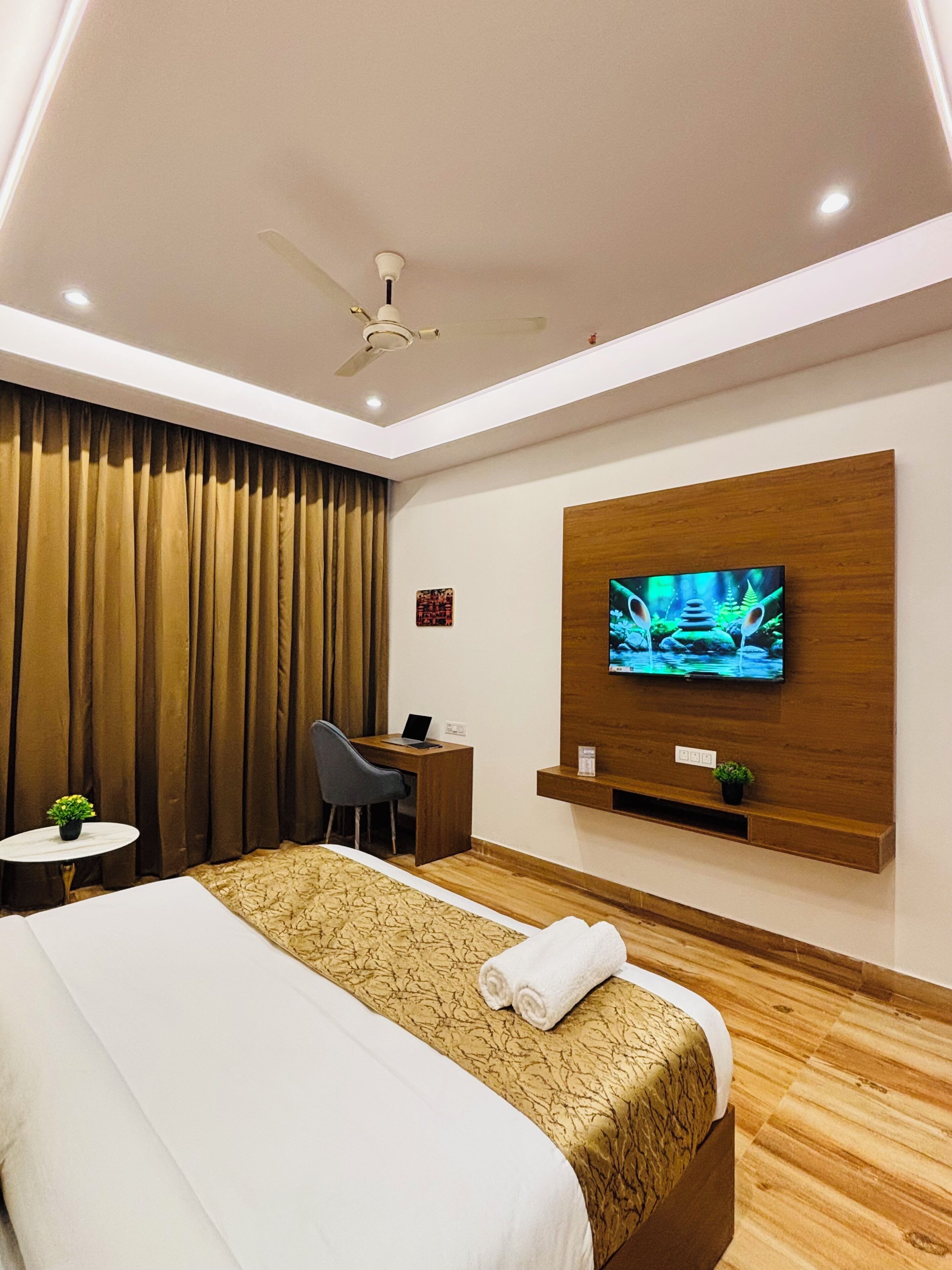 A hotel room with a bed, desk, chair, television, and a ceiling fan.