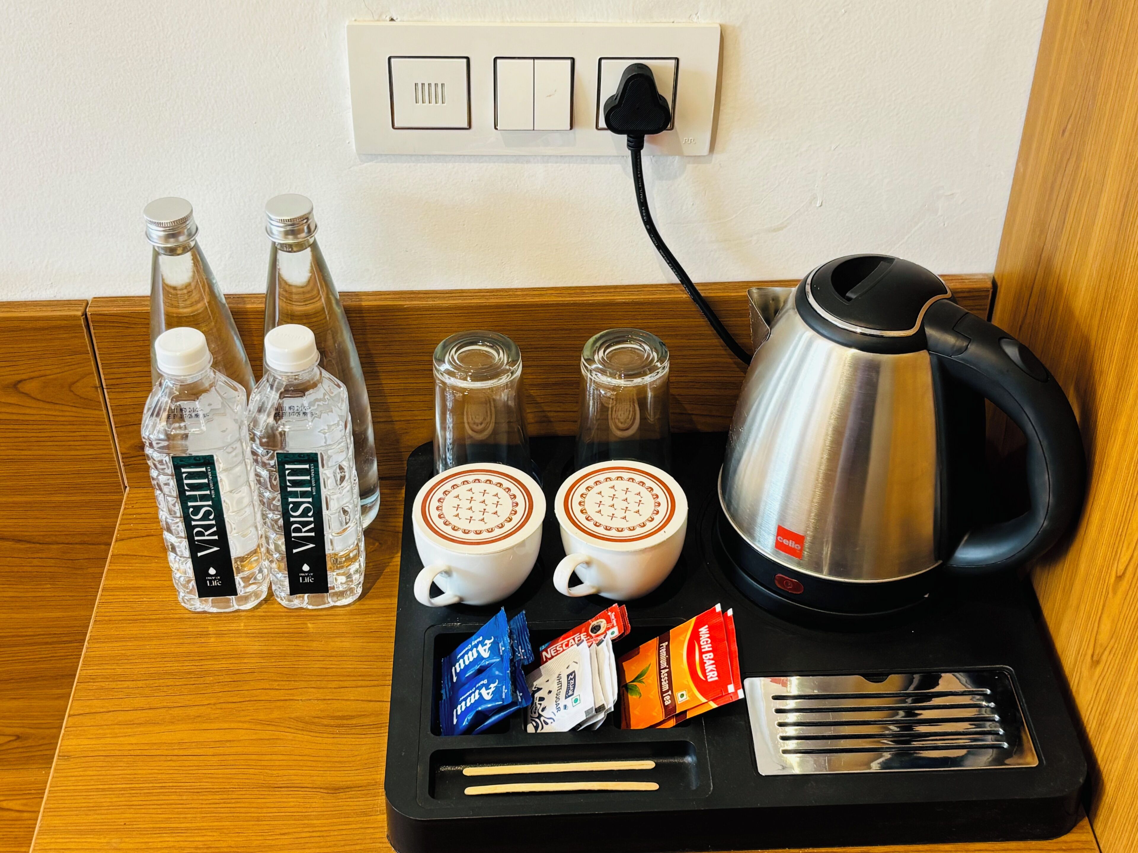 Un comptoir de cuisine avec une machine à café, deux bouteilles d’eau, deux verres, une bouilloire et quelques sachets de thé.