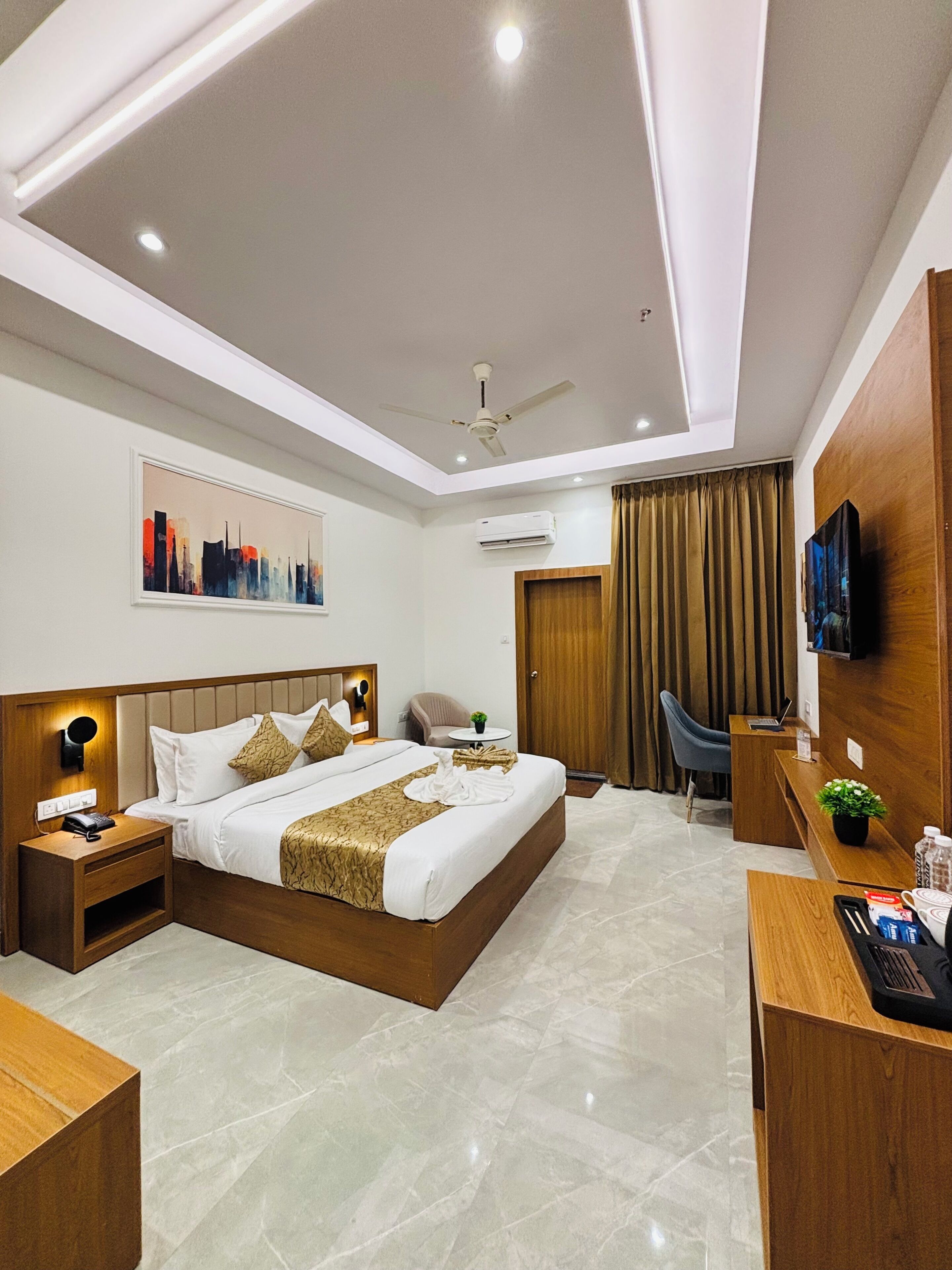 A modern hotel room with a large bed, a desk, a chair, a TV, and an air conditioning unit.