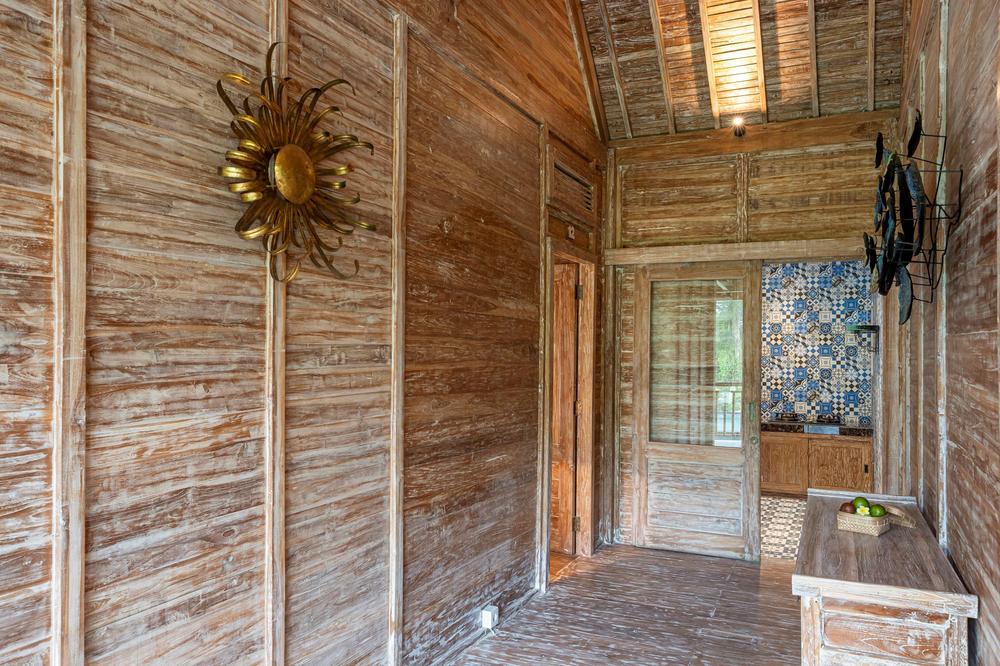A rustic wooden interior with a decorative sun on the wall, a tiled backsplash in the kitchen area, and a wooden bench with fruits.