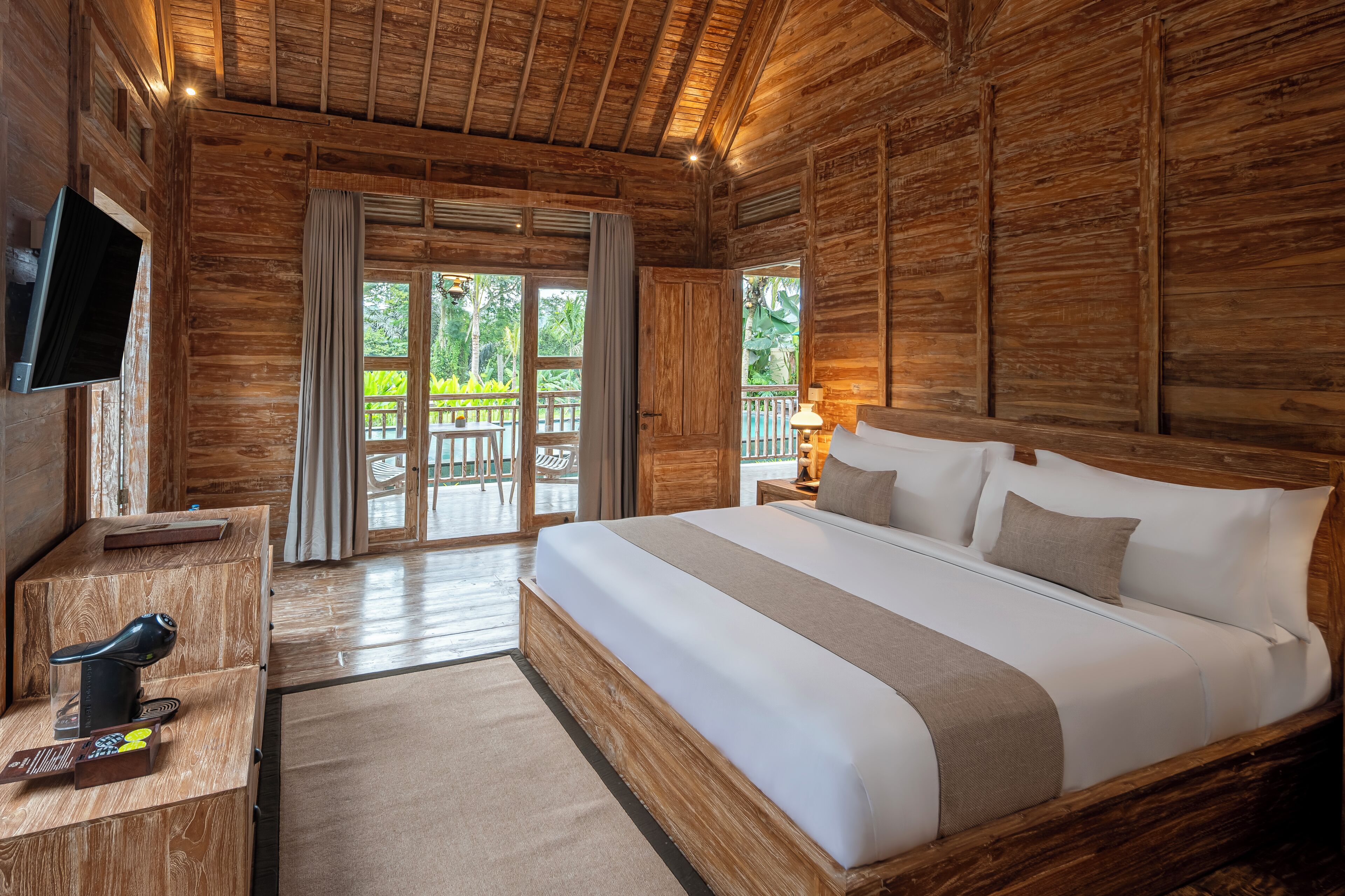 A wooden cabin-style bedroom with a large bed, a TV mounted on the wall, and a desk with a chair.