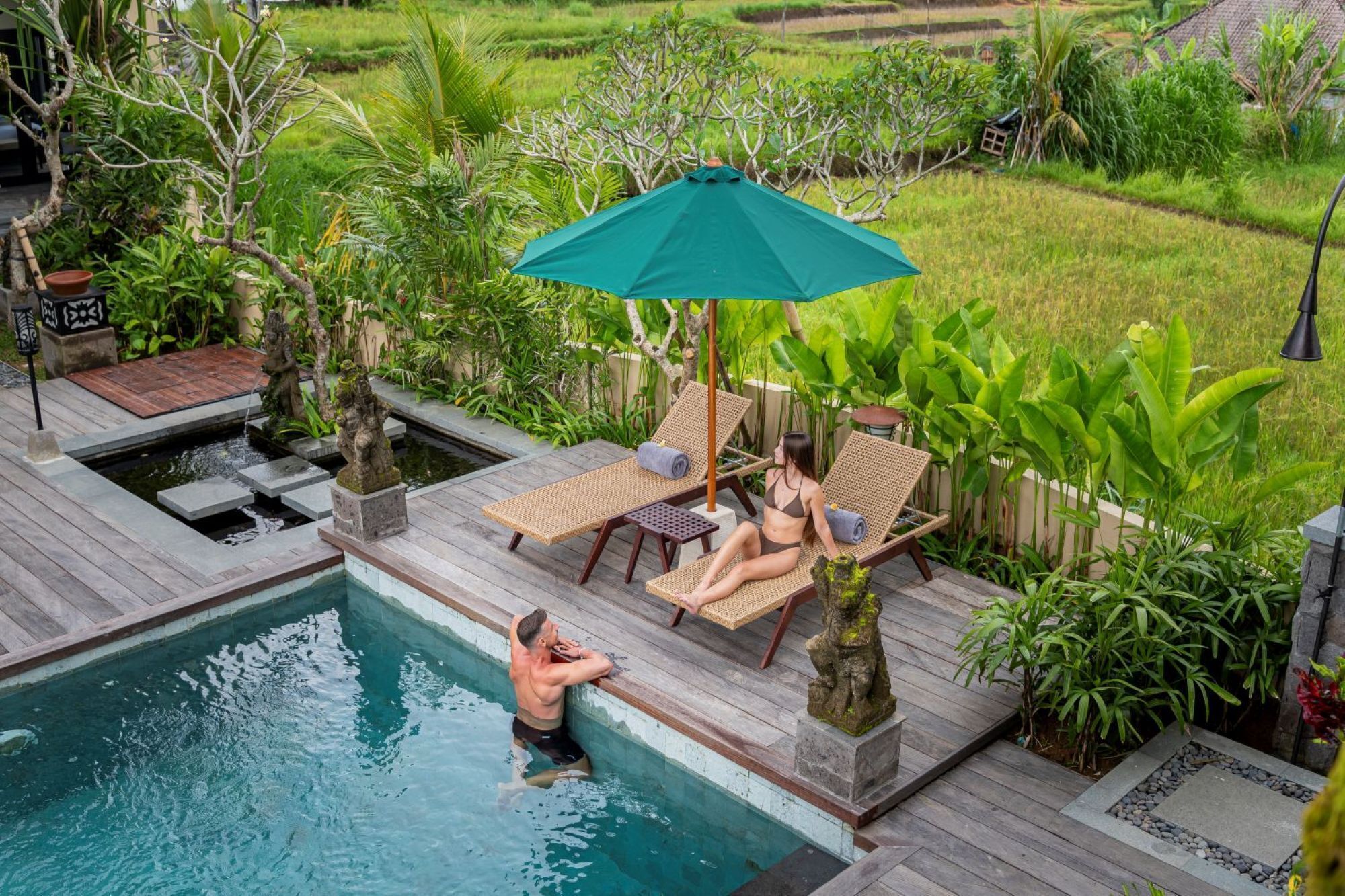 A pool area with a wooden deck, lounge chairs, and a green umbrella.