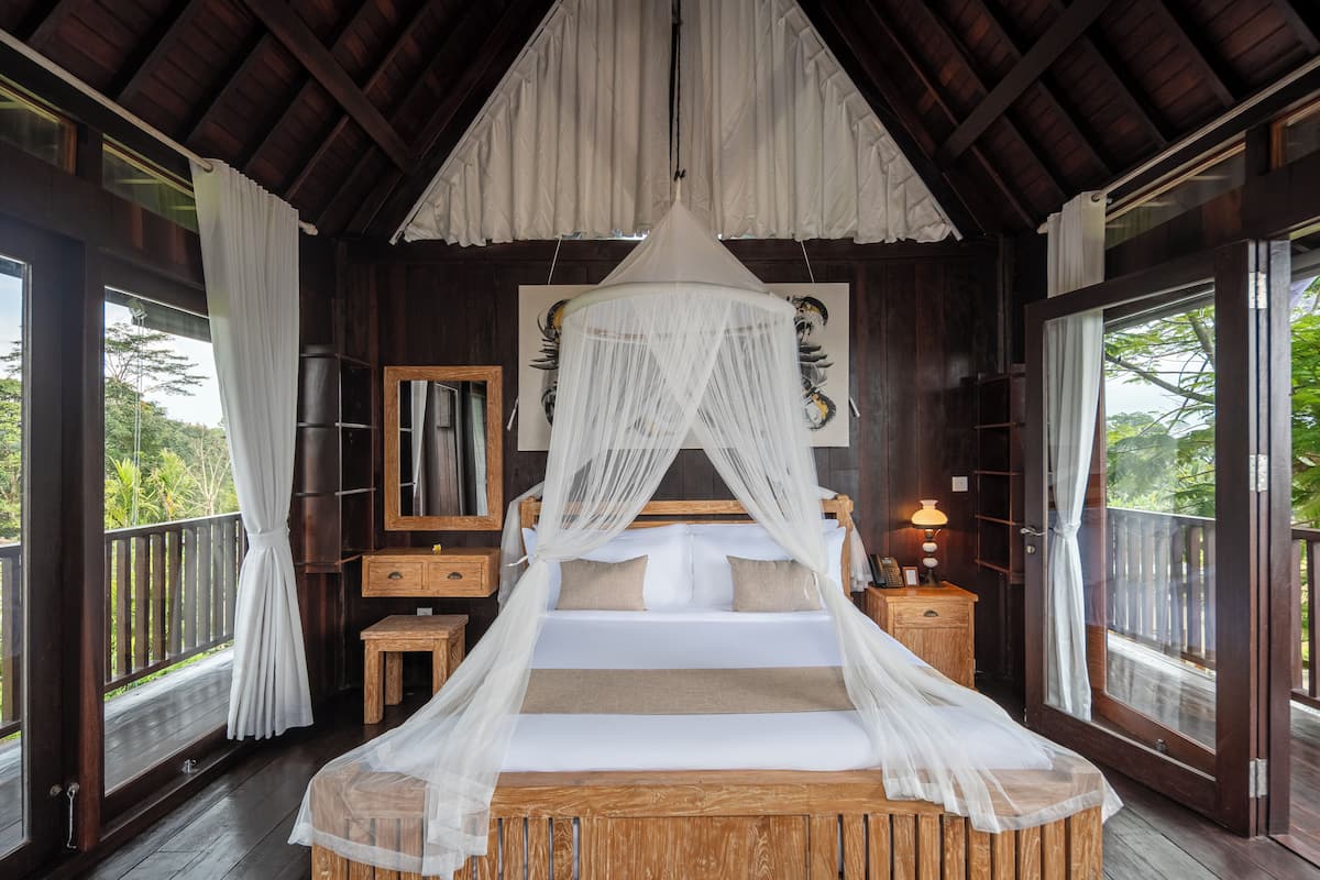 A bedroom with a canopy bed, wooden furniture, a nightstand, and a view of the outdoors.