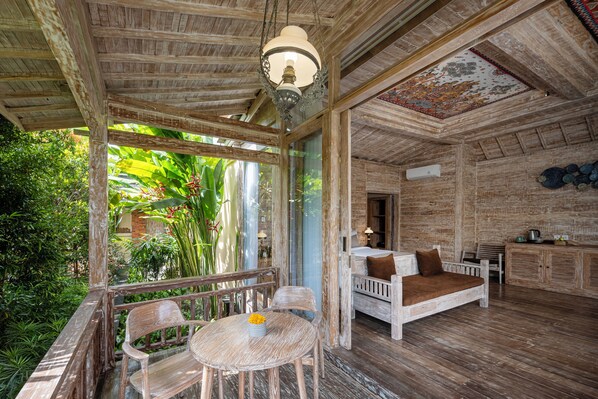 A wooden interior with a wooden ceiling, a hanging light fixture, a wooden bench, a table with a bowl of fruit, and a view of greenery outside. - Emana Abian Taksu (Payangan)